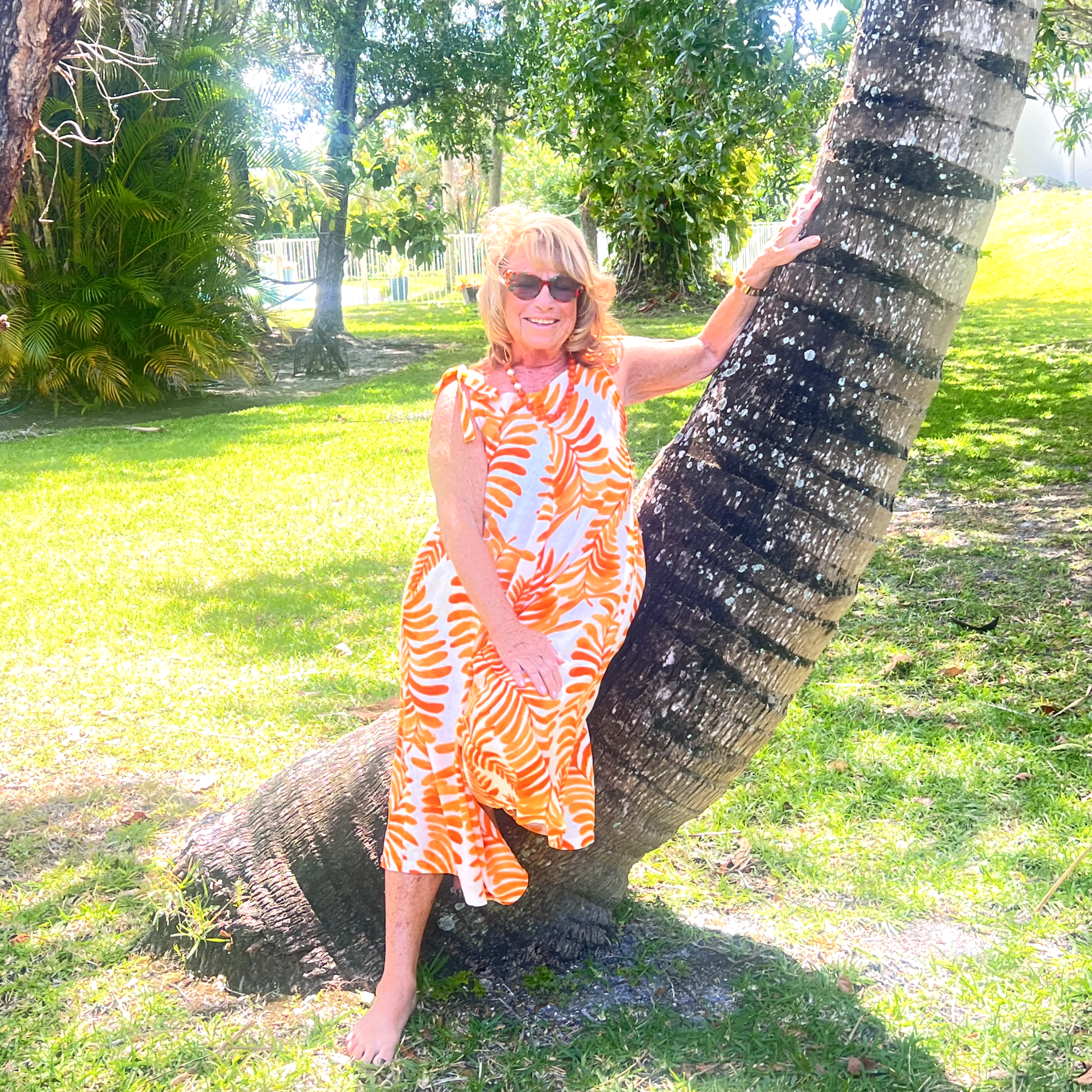 A woman in an orange and white dress leaning against a tree.